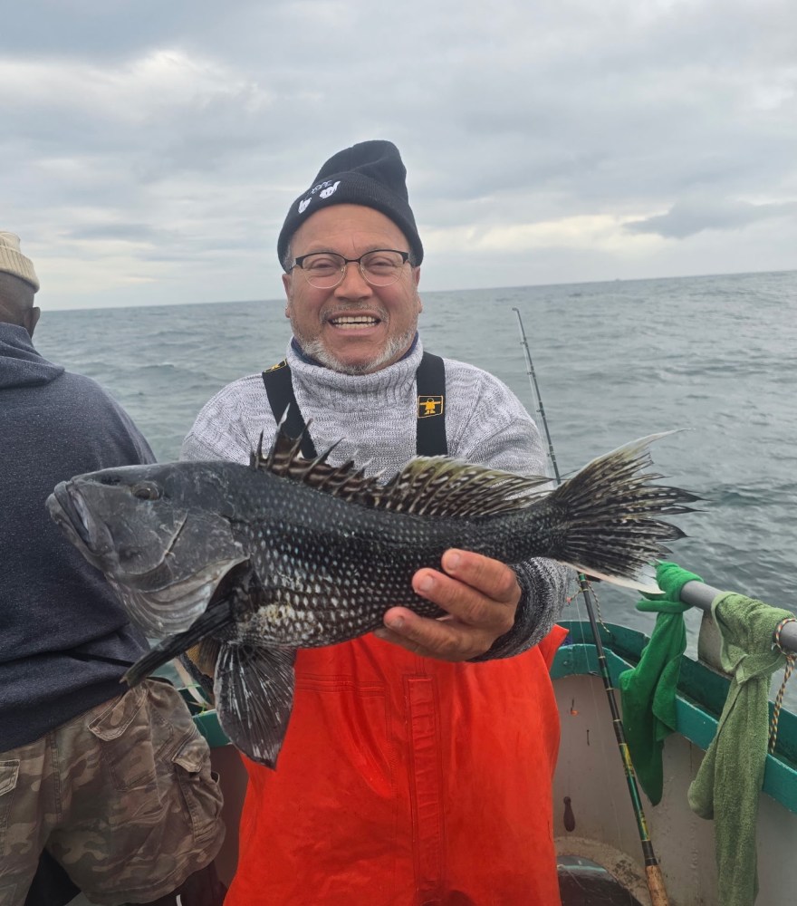Person in orange overalls holding a large fish on a boat at sea.