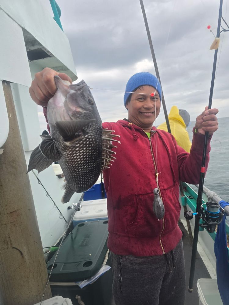 Person in red jacket holding a fish on a fishing boat, smiling with a cloudy sky background.