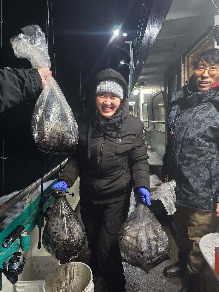 Person on boat holding bags of fish at night, smiling with another person.