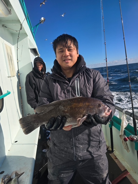 Person holding a large fish on a boat with another person and fishing rods visible.