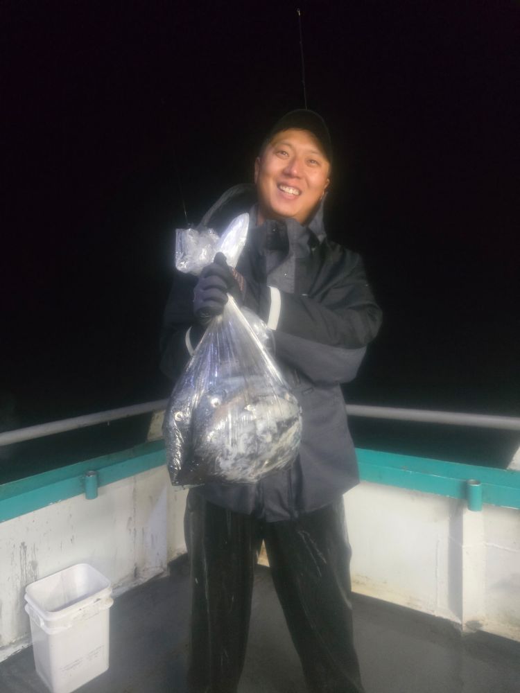 Person on a boat holding a fish in a plastic bag at night, smiling.