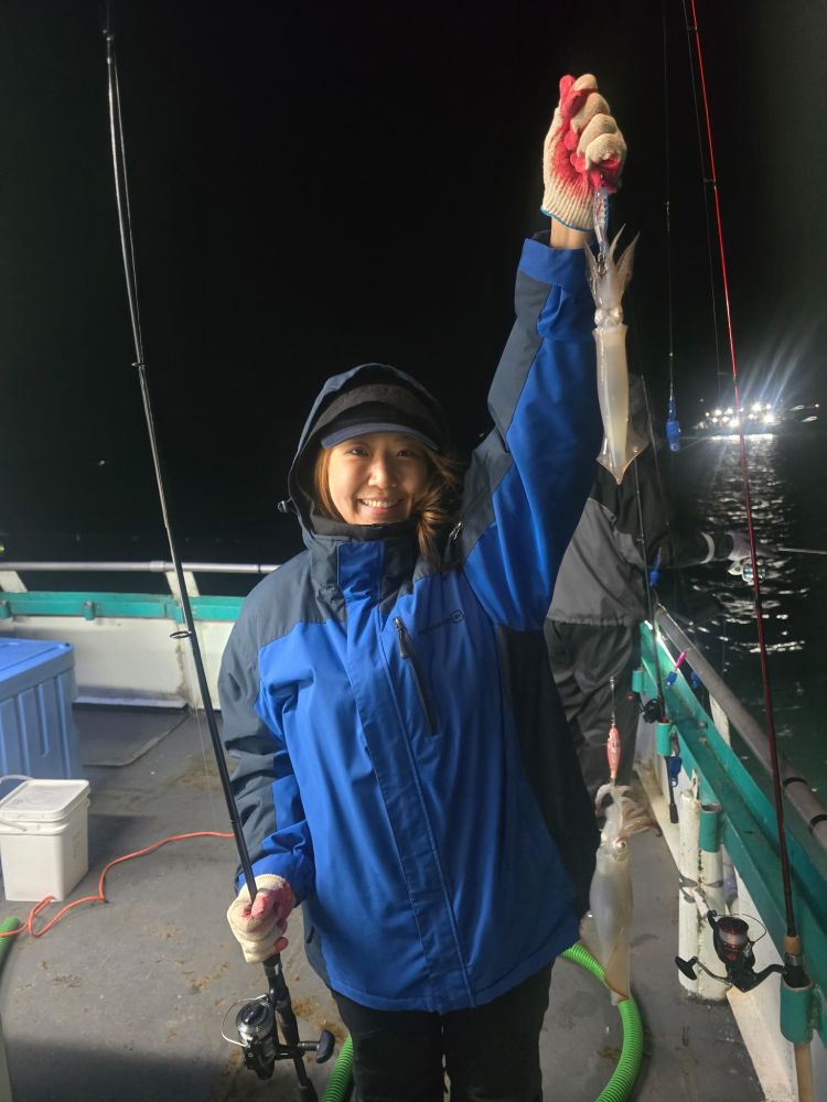 Person in blue coat holding a squid and a fishing rod on a boat at night.
