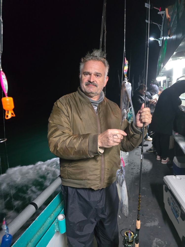 Man holding fishing rod with squid on boat at night.