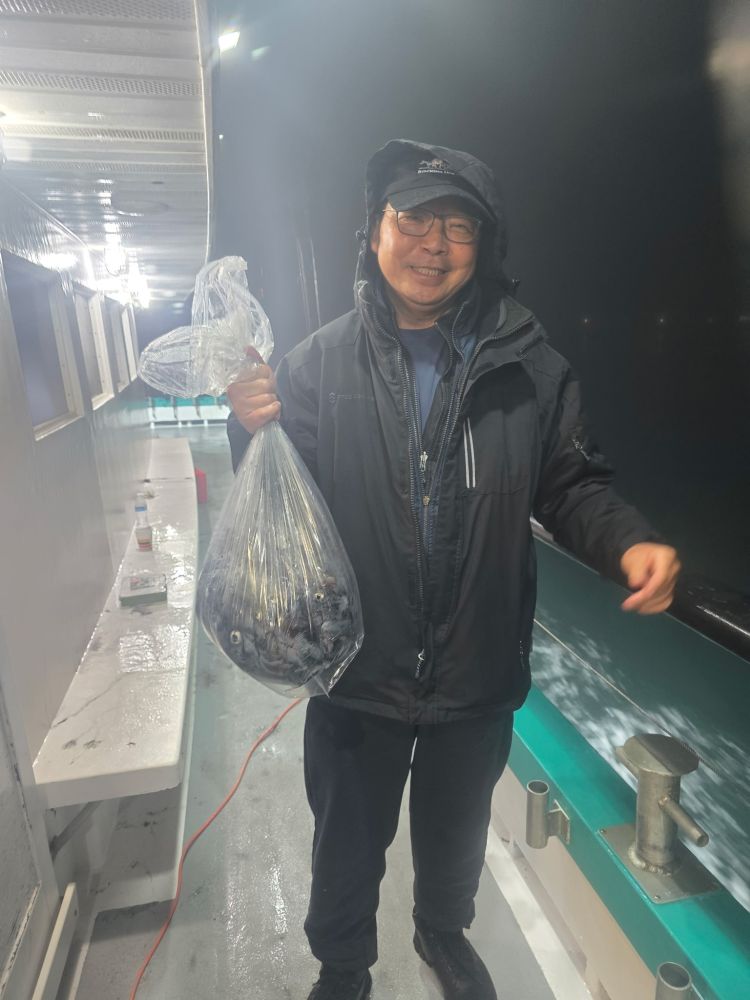 Person on a boat holding a bag of fish or octopus, wearing a hat and jacket, smiling.
