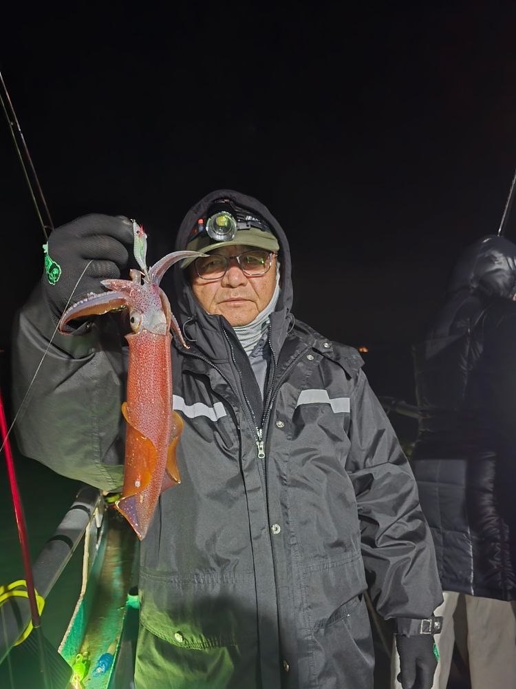Person holding a squid on a boat at night, wearing a headlamp and dark jacket.