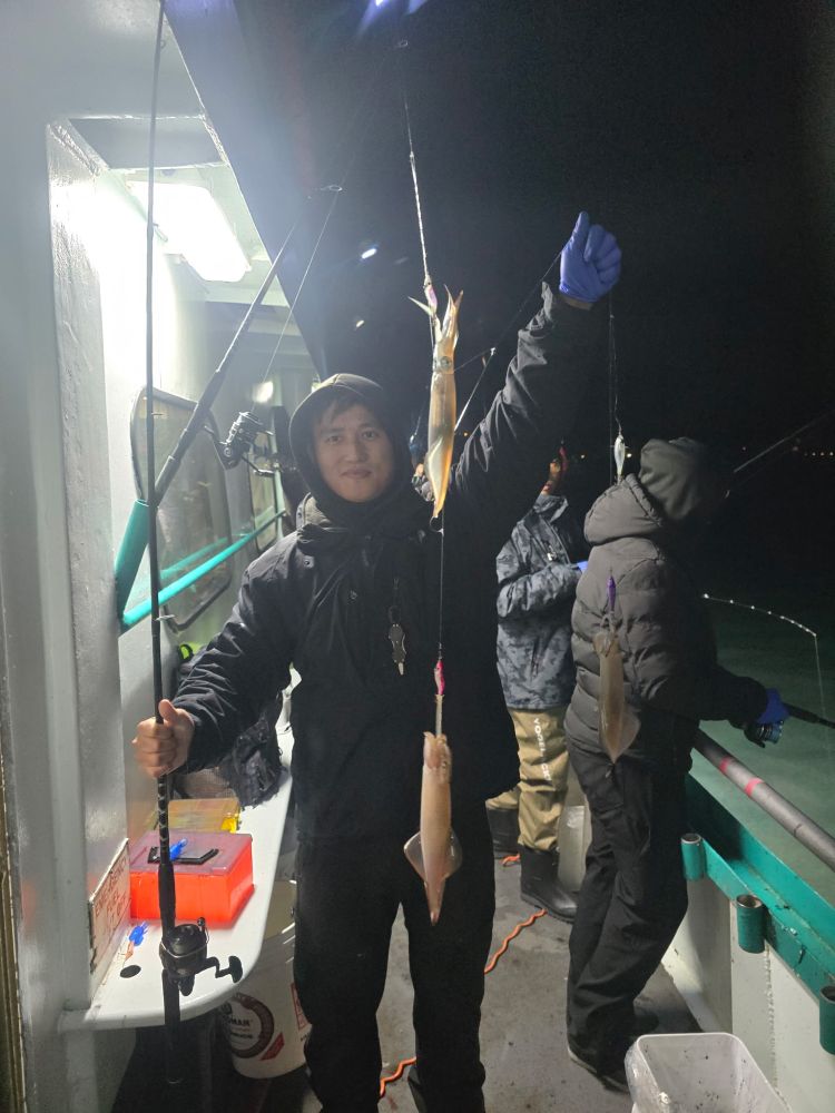 Person holding a fishing rod with squid, standing on a boat at night.