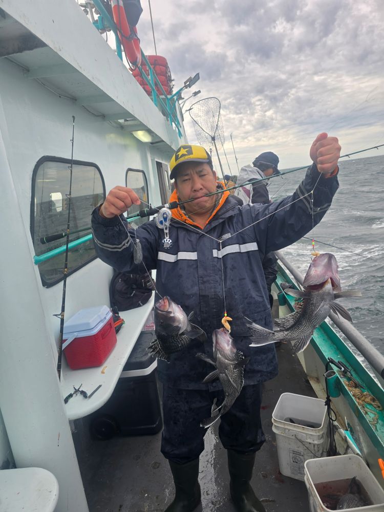 Person holding three fish on a line aboard a boat at sea, with fishing gear around.