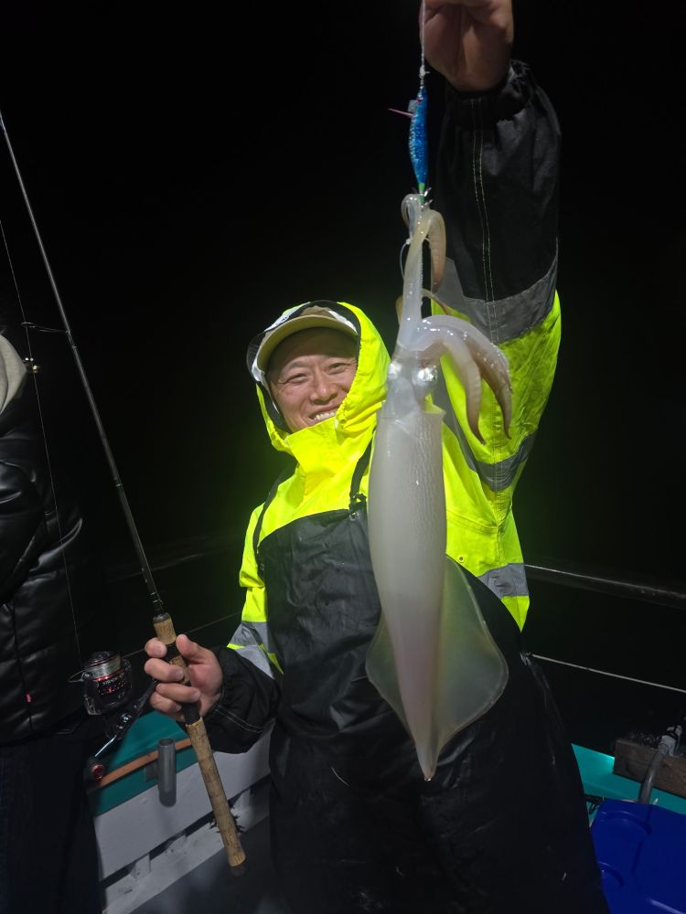Person in yellow raincoat holding a squid on a boat at night.