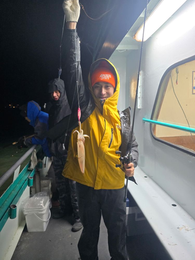 Person in a yellow jacket holds a squid and fishing pole on a boat at night.