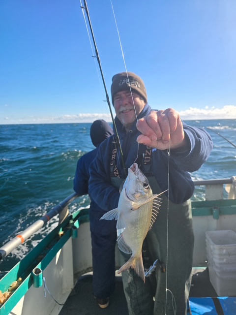 Man on a boat holding a fish with the sea in the background.