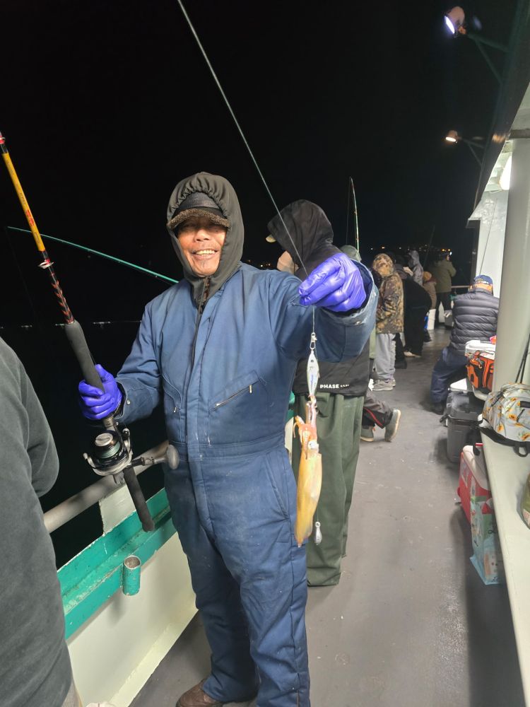 Person in blue suit holding a fishing rod and a squid on a boat at night.