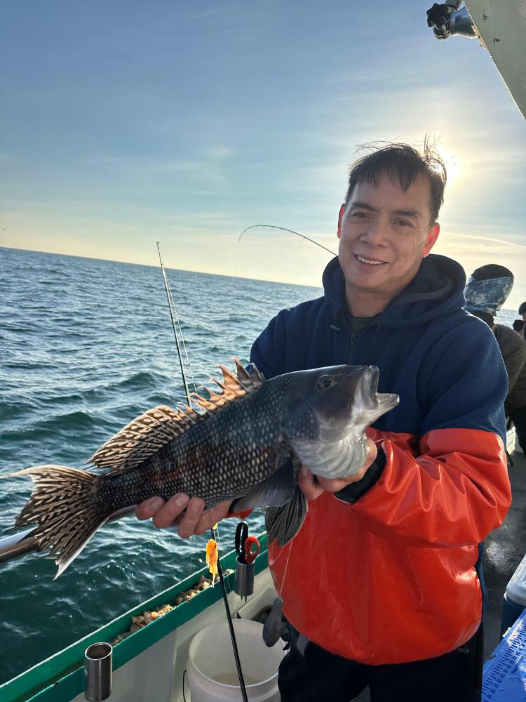 Person holding a large fish on a boat with ocean and sky in the background