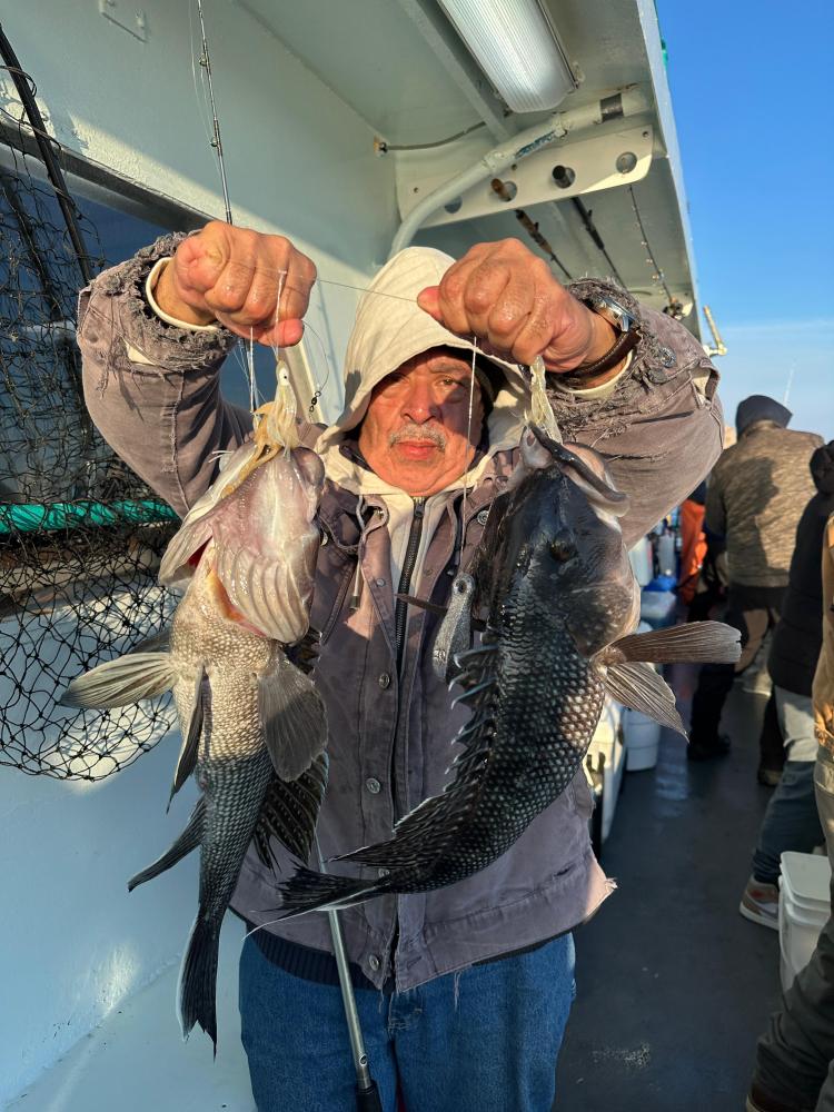 Person holds two large fish on a boat, wearing a hoodie and jacket.