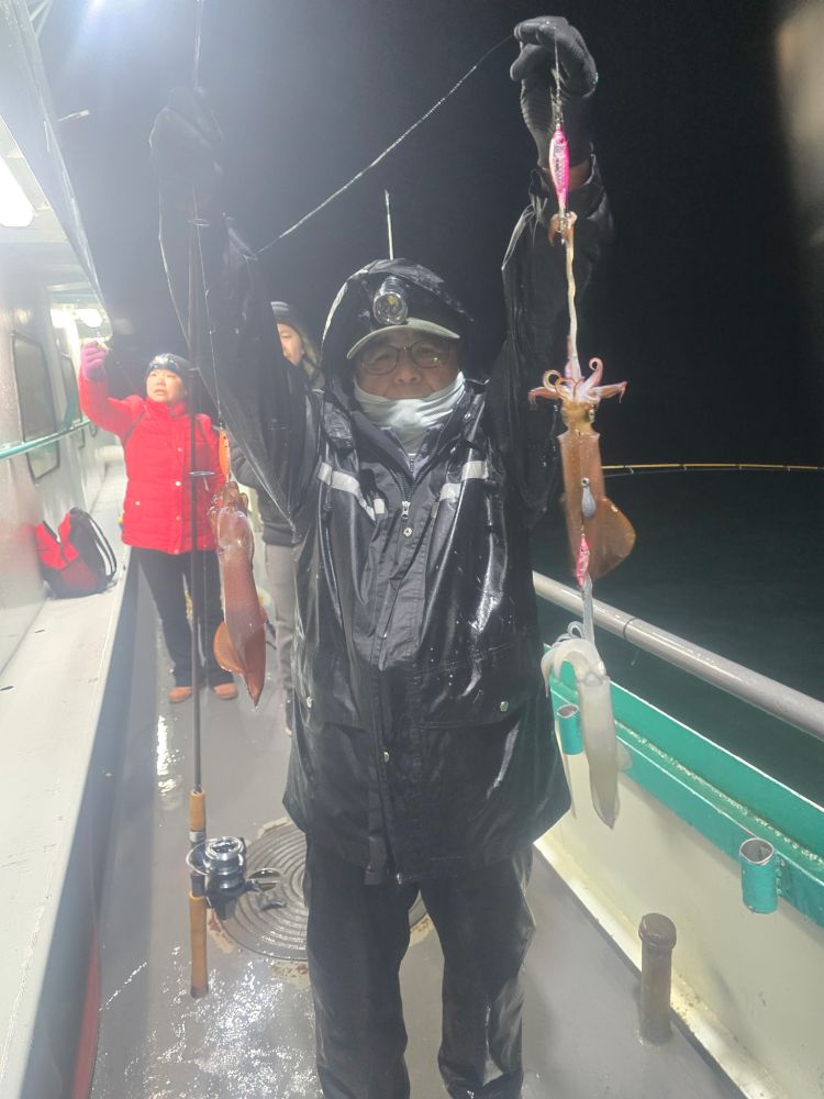 Person on boat holding multiple squid in rainy nighttime setting.