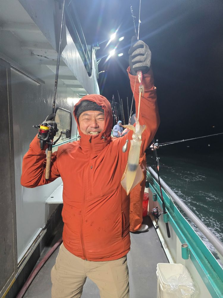 Person in orange jacket holding a squid on a fishing line on a boat at night.