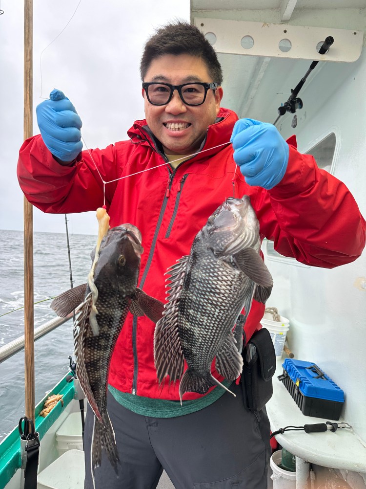 Person in red jacket holding two black fish on a boat.