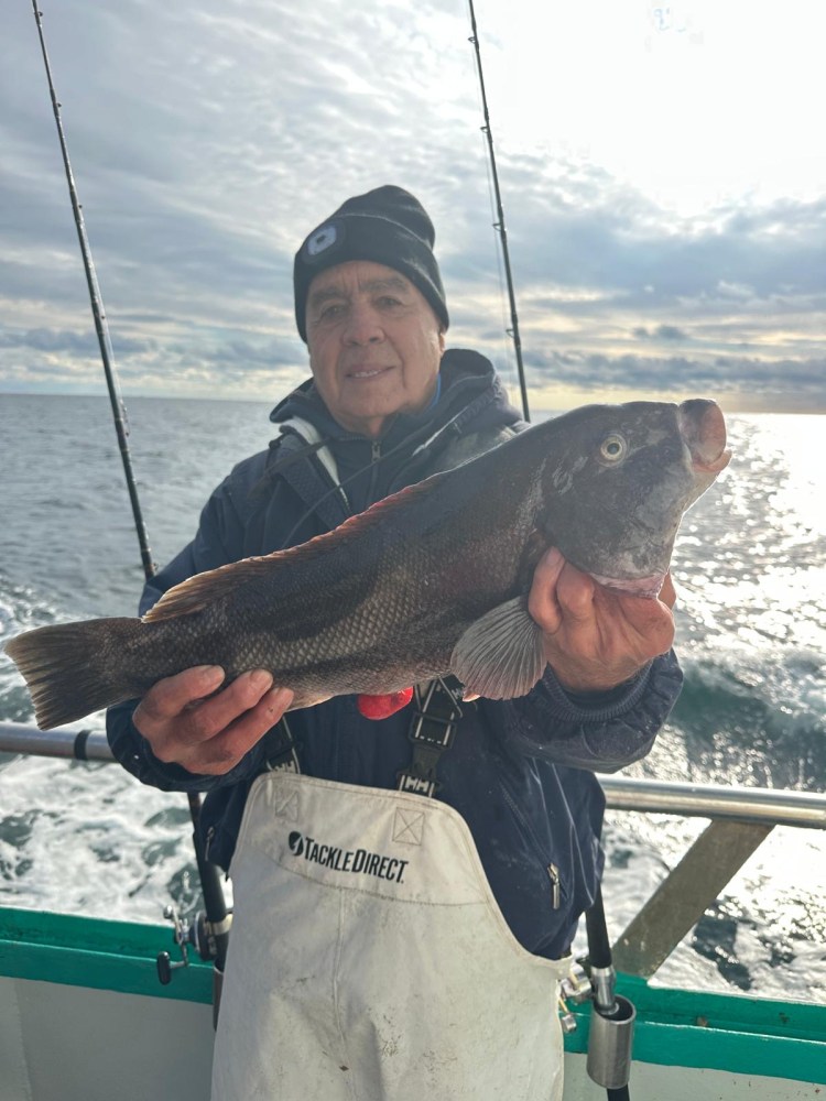 Person holding a large fish on a boat with a cloudy sky and ocean in the background.
