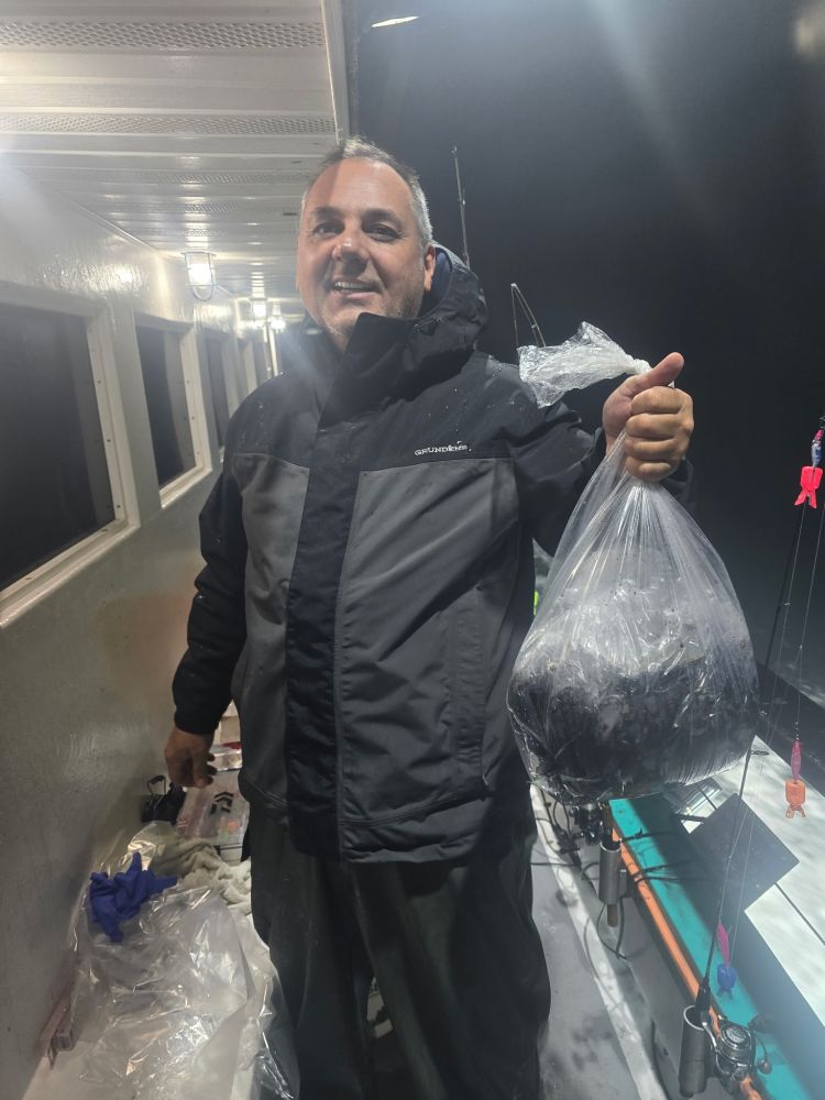 Man on a boat at night holding a bag of fish.