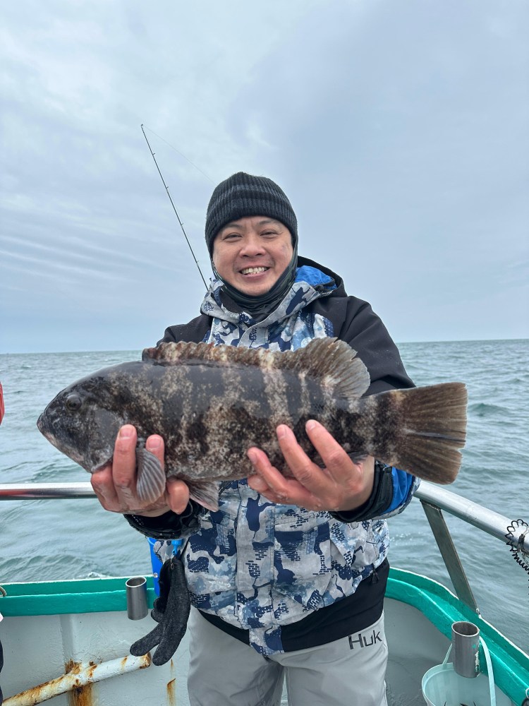 Person on a boat holding a large fish, wearing a beanie and a camouflage jacket.