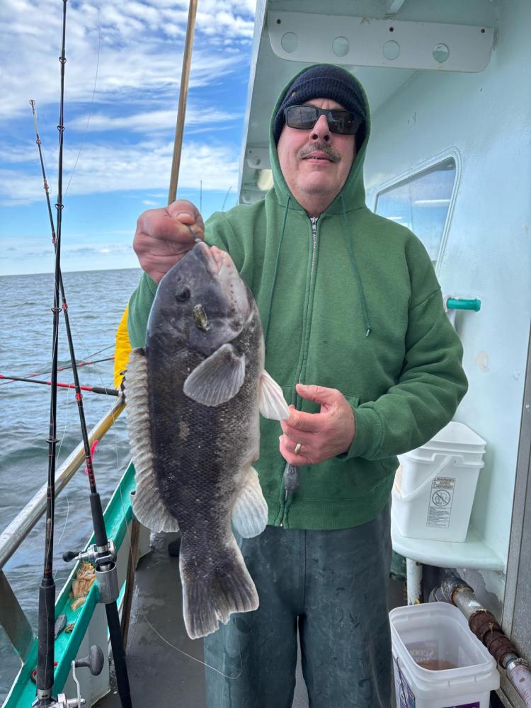 Person in green hoodie holding a large fish on a boat under a cloudy sky.