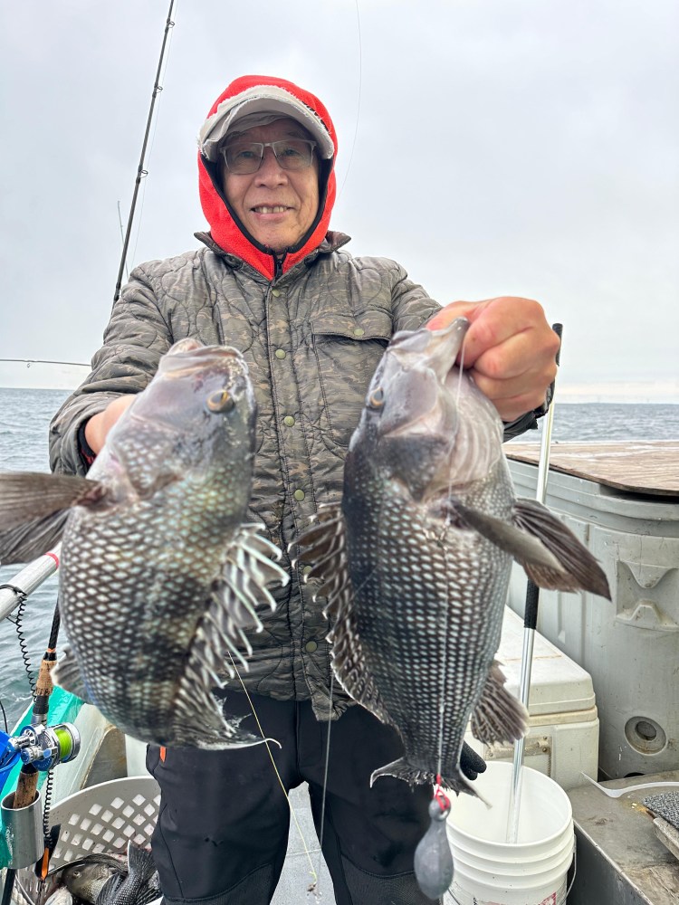 Person in winter clothing holding two fish on a boat with fishing gear nearby.