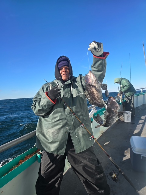 Person holding two fish on a boat with another person in the background.