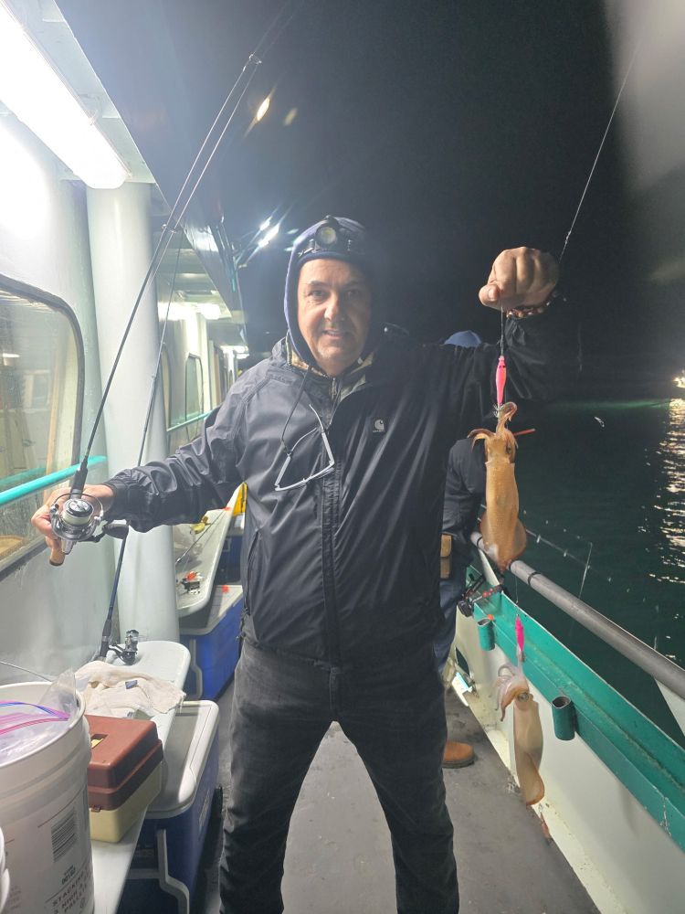 Person on a boat at night holding a fishing rod and a squid.