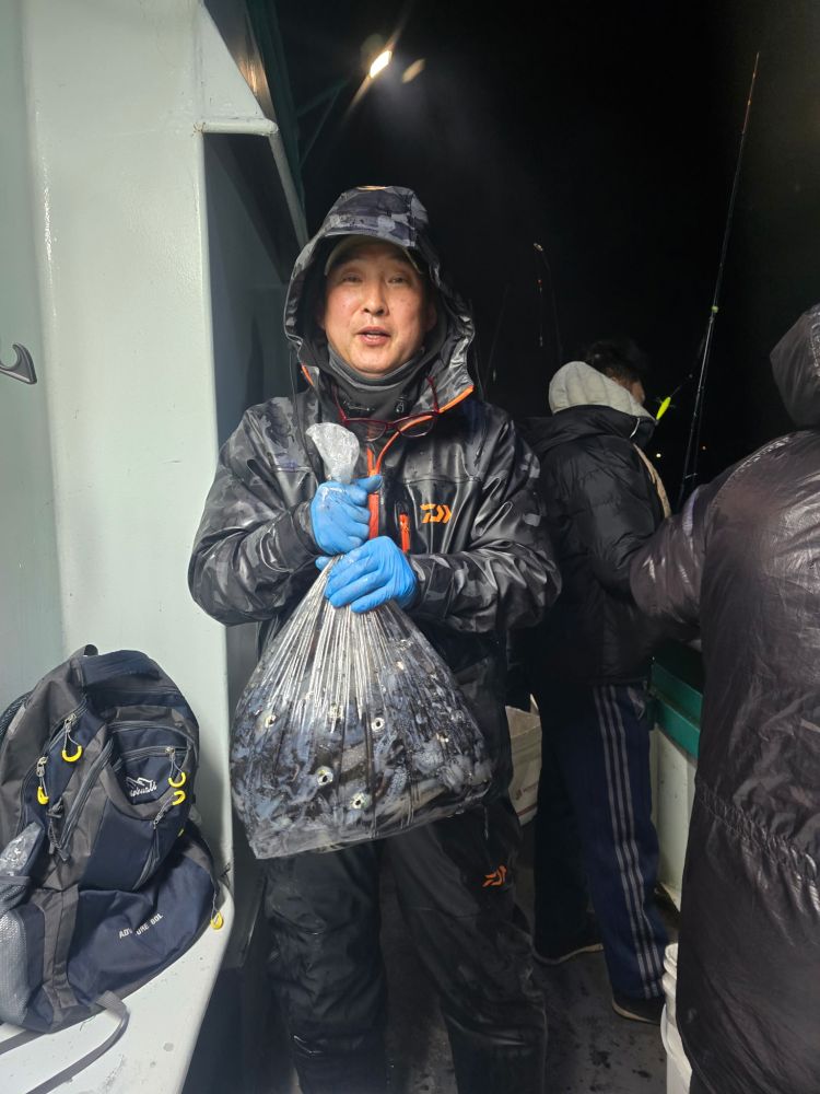 Person holding a bag of fish on a boat at night, wearing a hooded raincoat and gloves.