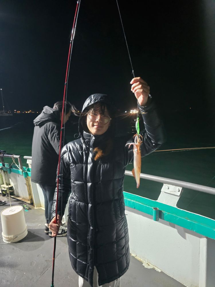 Person holding a fishing rod with a squid at night on a boat deck.