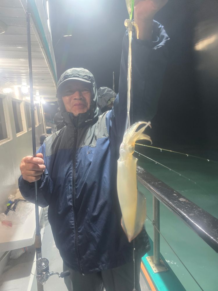 Person in raincoat holding a fishing rod and a freshly caught squid on a boat at night.