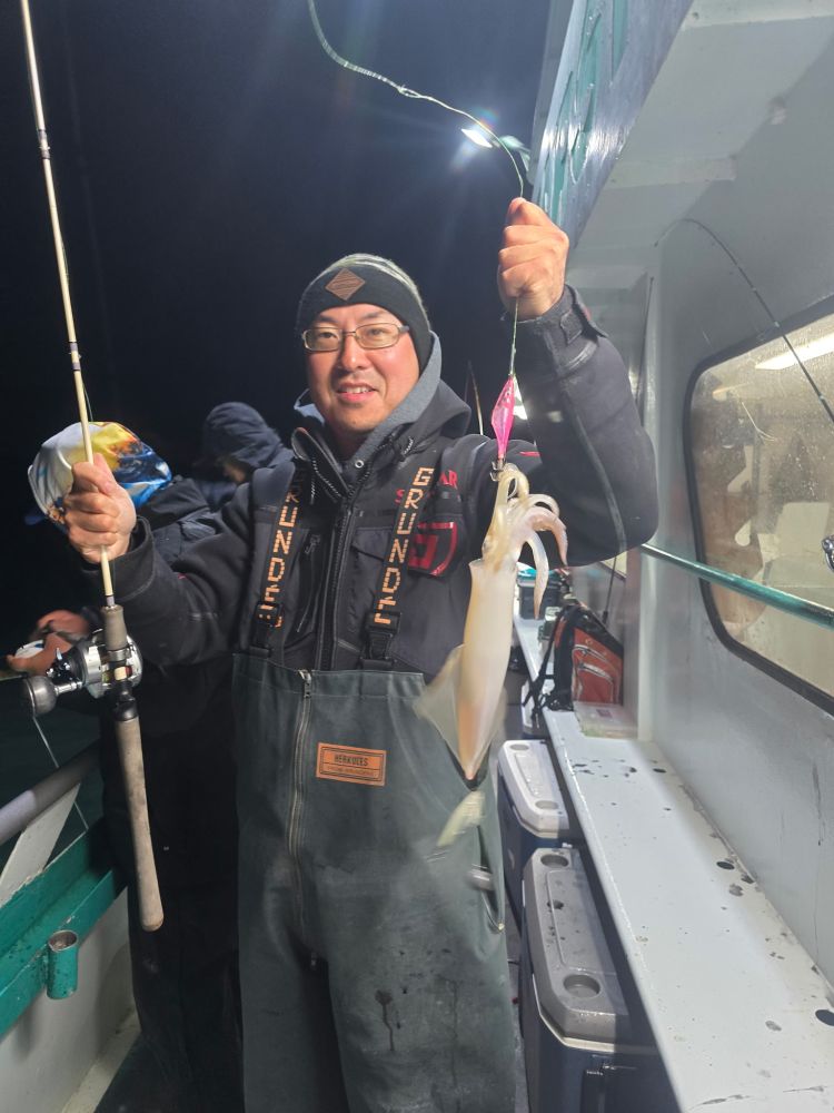 Person on boat holding a fishing rod with a squid caught on the line, wearing a hat and glasses.
