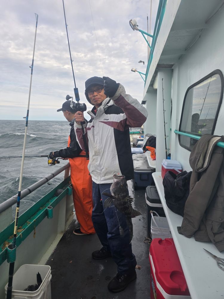 Two people fishing on a boat; one holds a fish caught with a rod.
