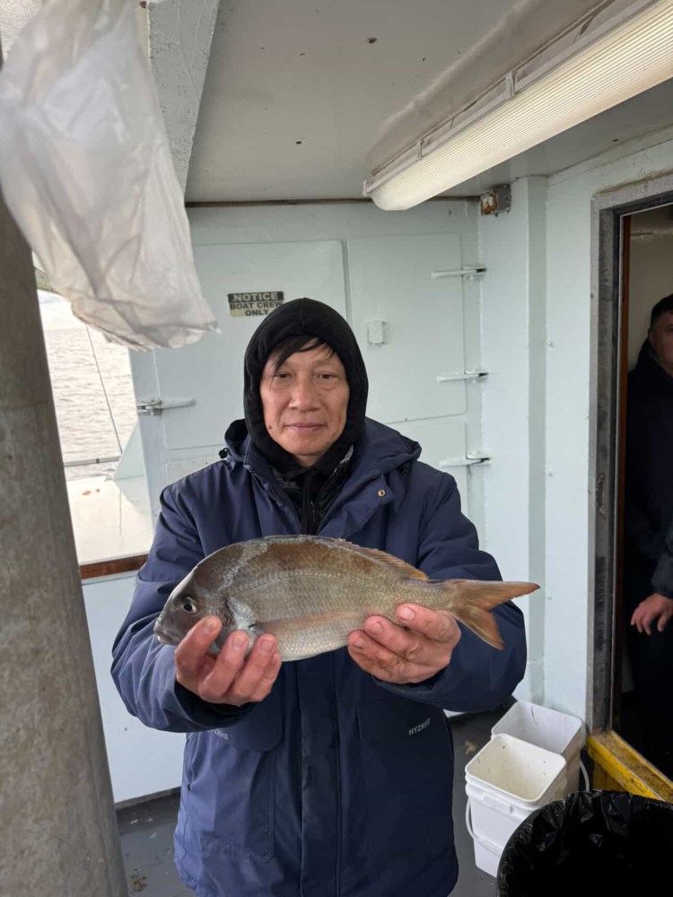 Person in a hooded jacket holding a fish on a boat.