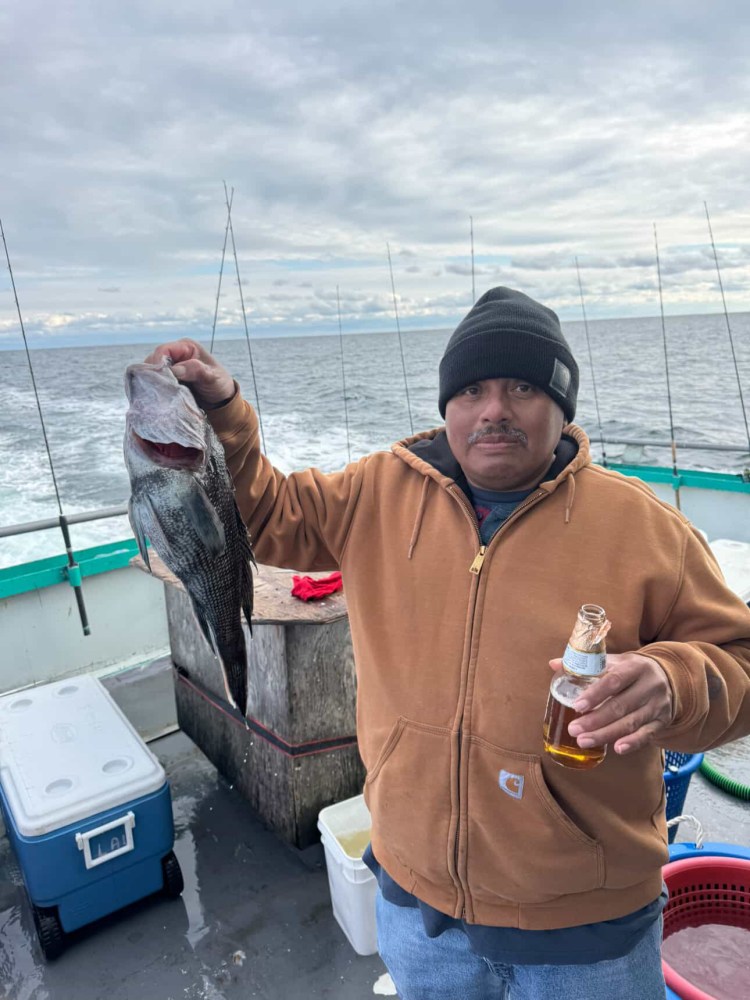 Person on a boat holding a fish in one hand and a bottle in the other.