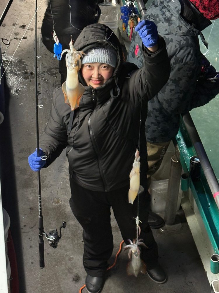 Person in winter clothing holding two caught squids on a fishing line indoors.
