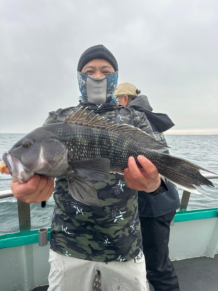 Person on boat holding a large fish, wearing a camo shirt and face covering.