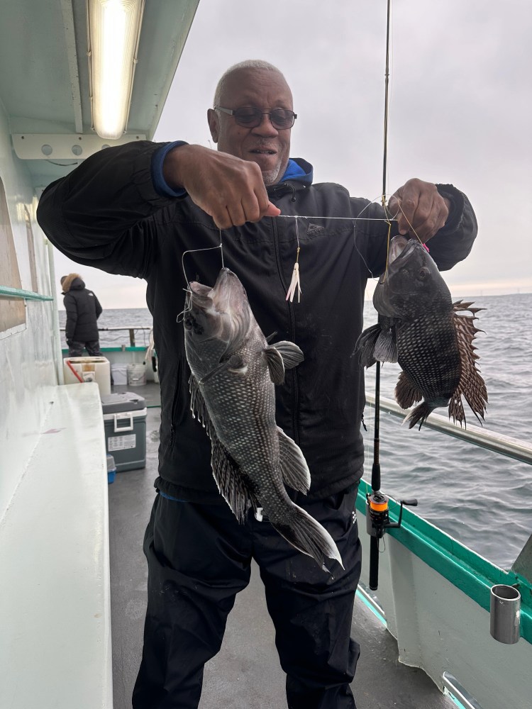 Person on boat holding two fish with a fishing rod, ocean in background.