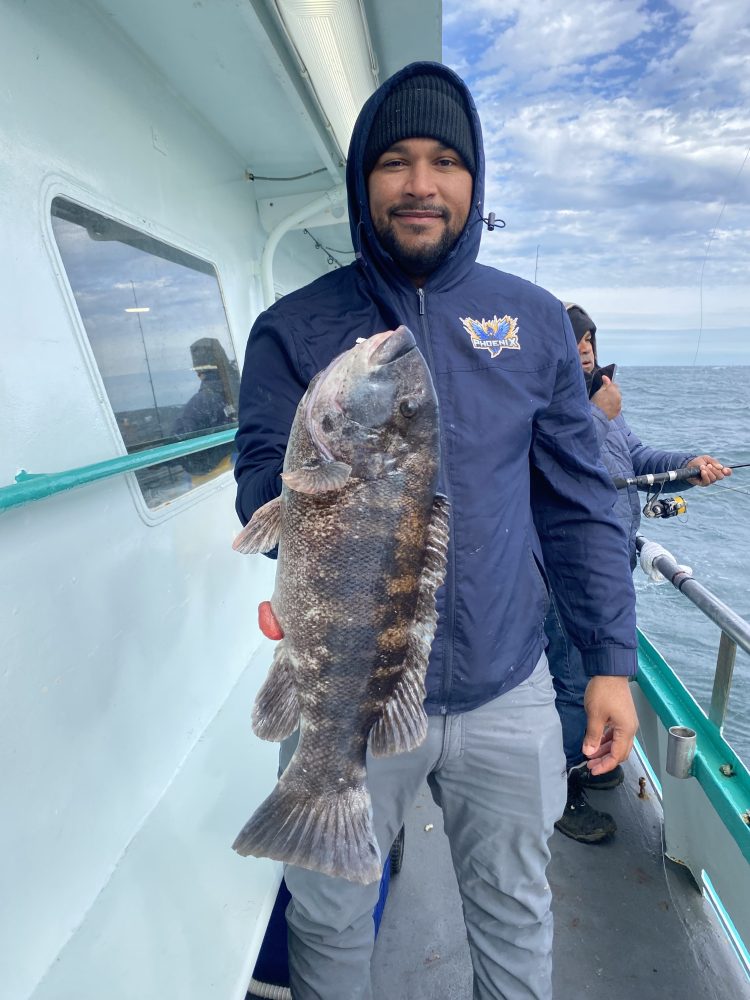 Person in a blue jacket holding a large fish on a boat with others fishing nearby.