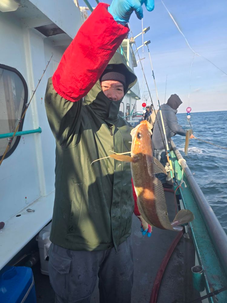 Person in winter clothing holding a fish on a boat with ocean in the background.