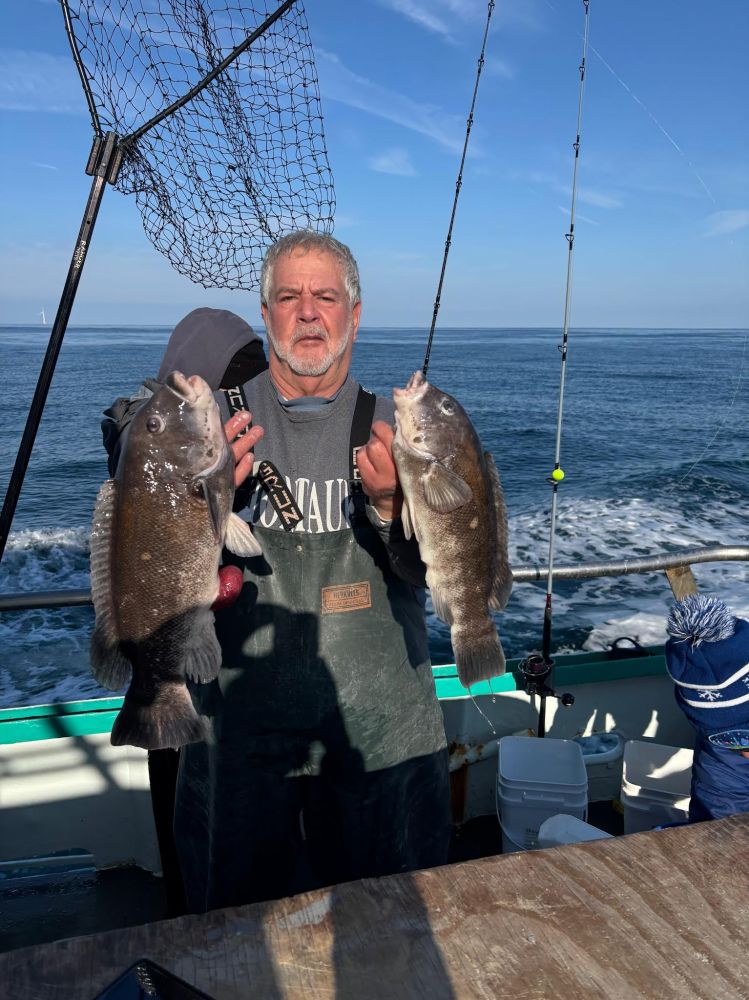 Man on boat holding two large fish with a fishing net in the background, ocean view.