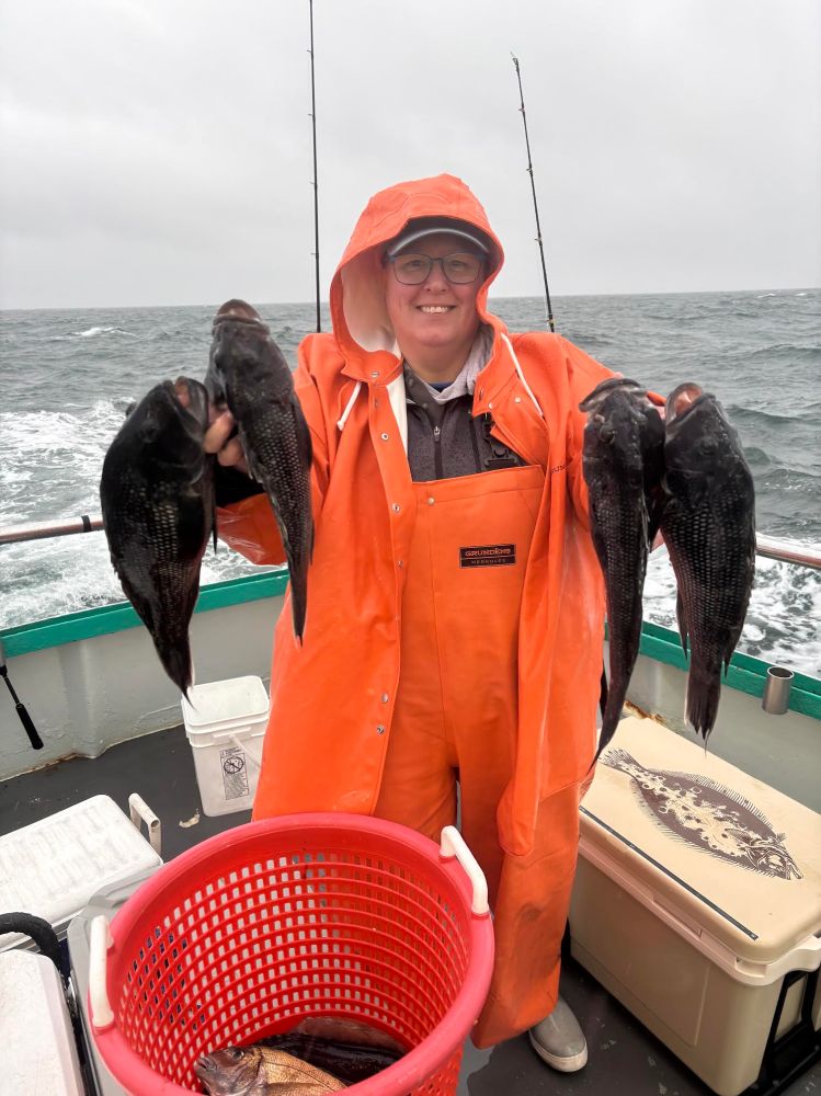Person in orange rain gear holding fish on a boat with ocean background.