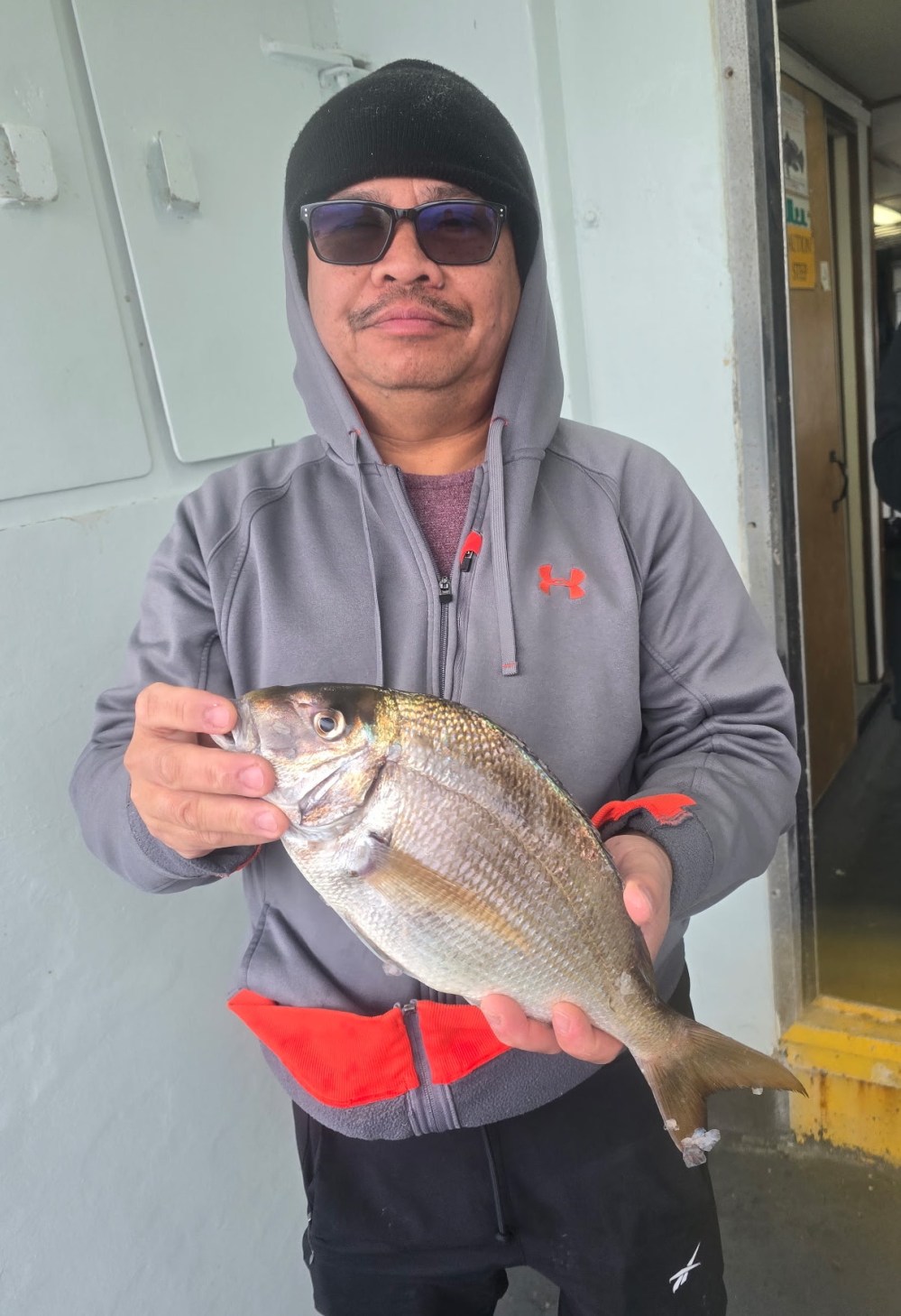 Person in gray hoodie holding a fish on a boat.