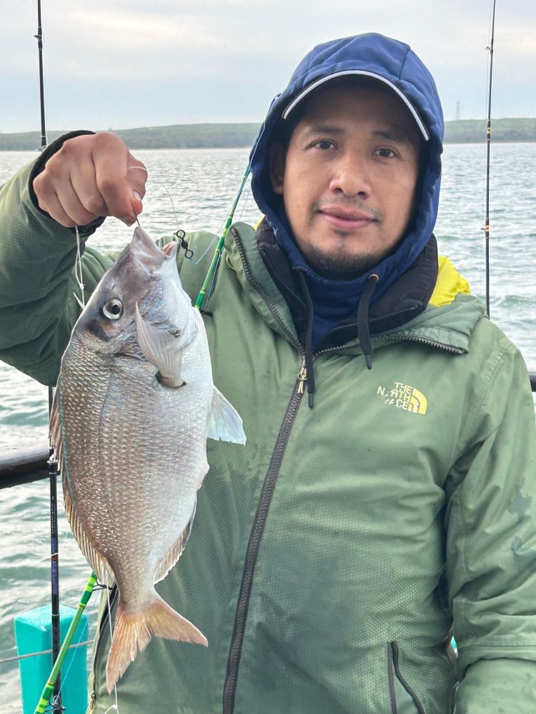 Person holding a fish on a boat, wearing a green jacket and blue hood.