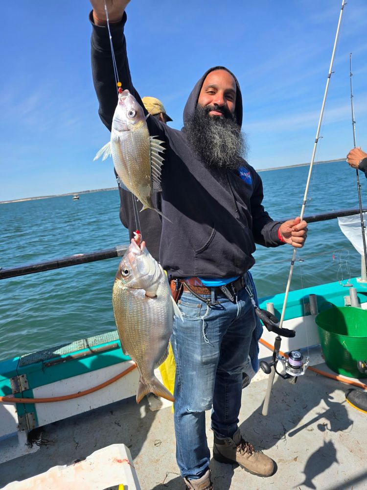 Man on boat holding two fish with a fishing rod.