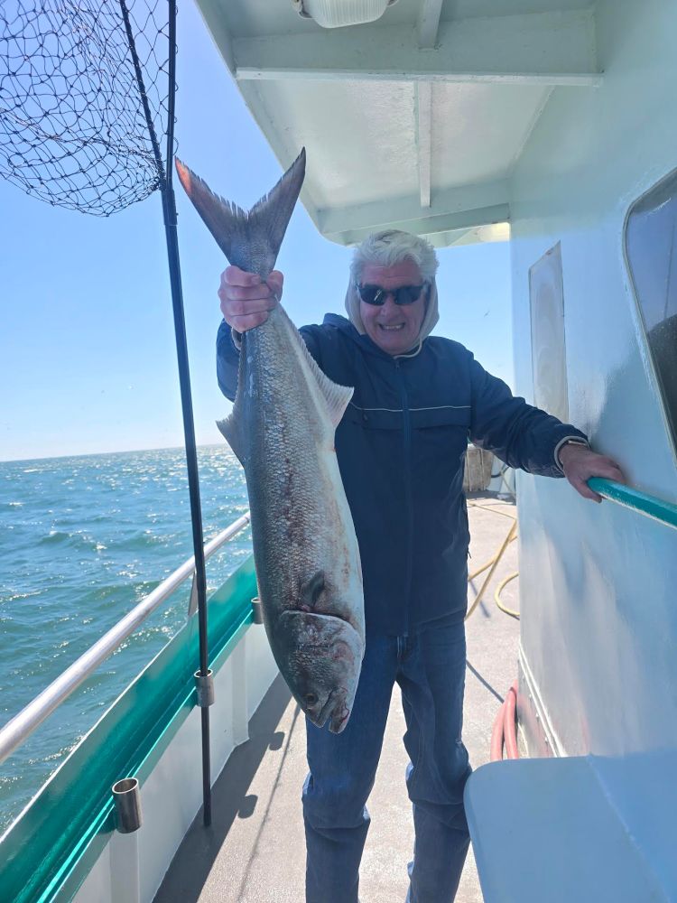 Man on a boat holding a large fish with a fishing net nearby.