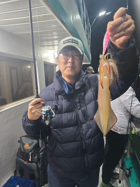 Person holding a fishing rod and large squid on a boat at night.