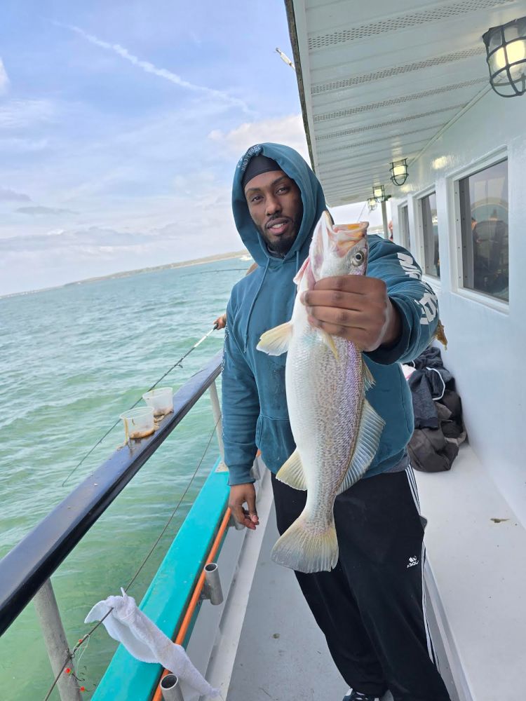 Person holding a fish on a boat deck with ocean in the background.