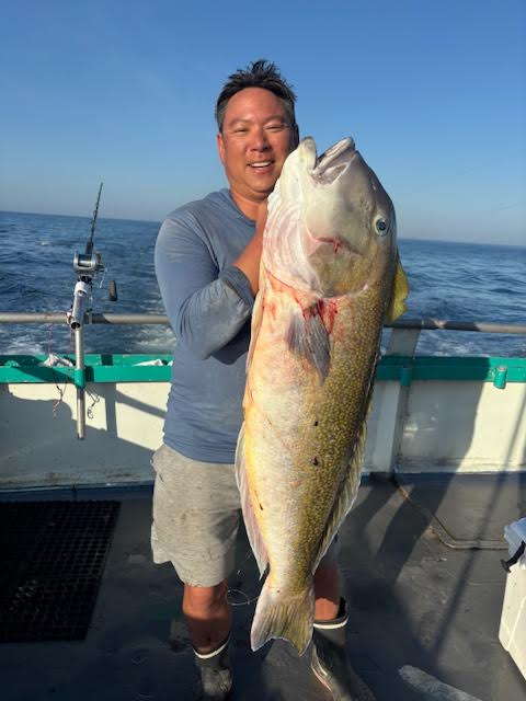 Person smiling while holding a large fish on a boat.