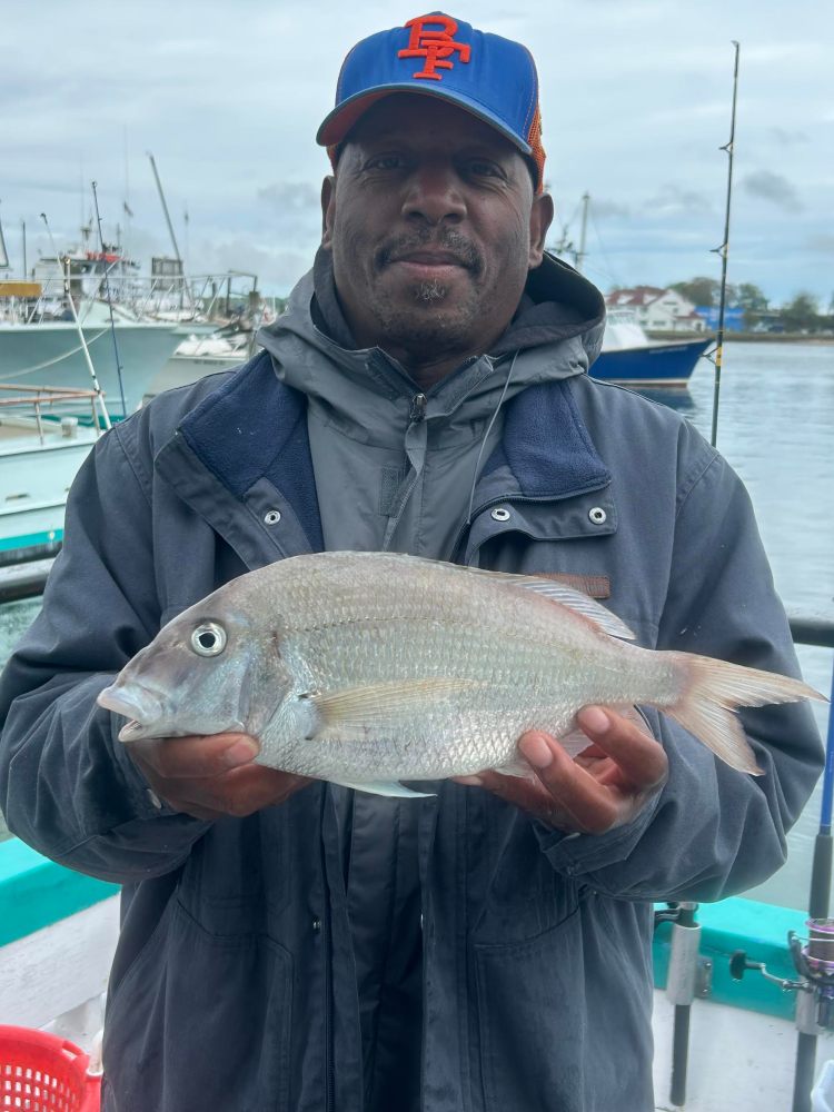 Man holding fish on a boat with harbor background.