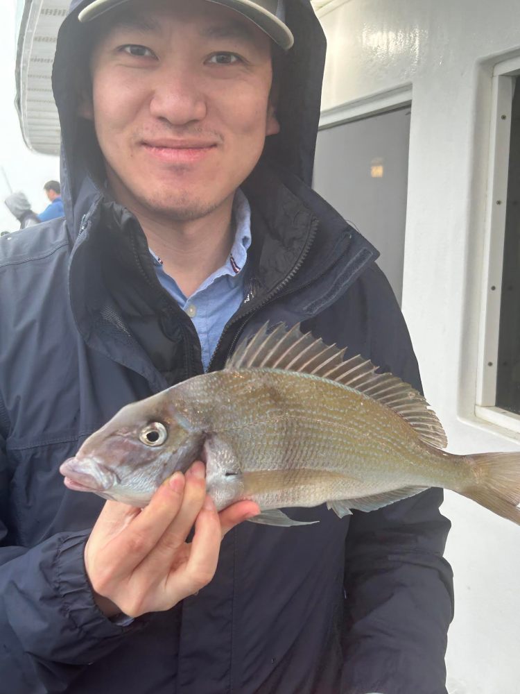 Person in a jacket and cap holding a fish on a boat.